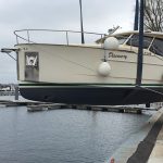 Cremefarbene Motoryacht in einem Hafen, am Kran aufgehängt, ein Bootsführer hält eine Halteleine