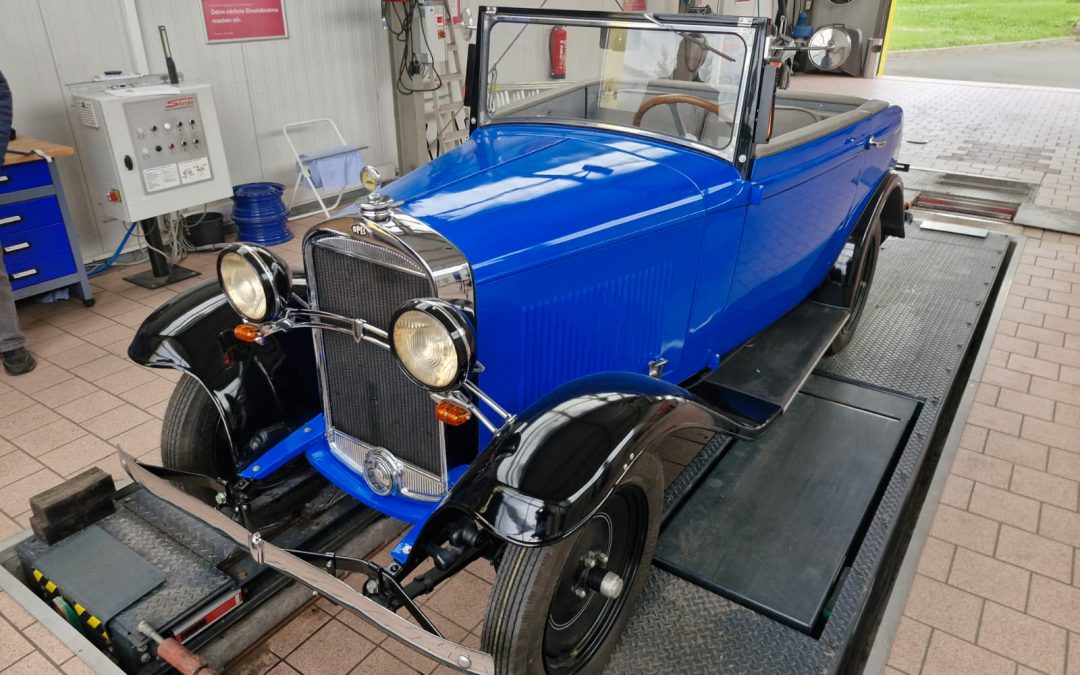Koenigsblauer Opel Adam Cabriolet von 1934 mit schwarzen Kotfluegeln, Cabrio offen, steht auf einem HU-Pruefstand
